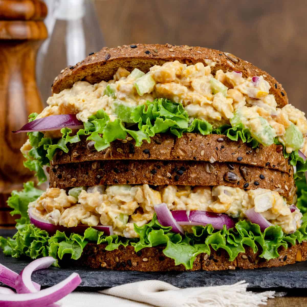 Closeup of two sandwiches stacked on top of each other filled with a mock tuna chickpea of the sea filling on hearty brown bread.