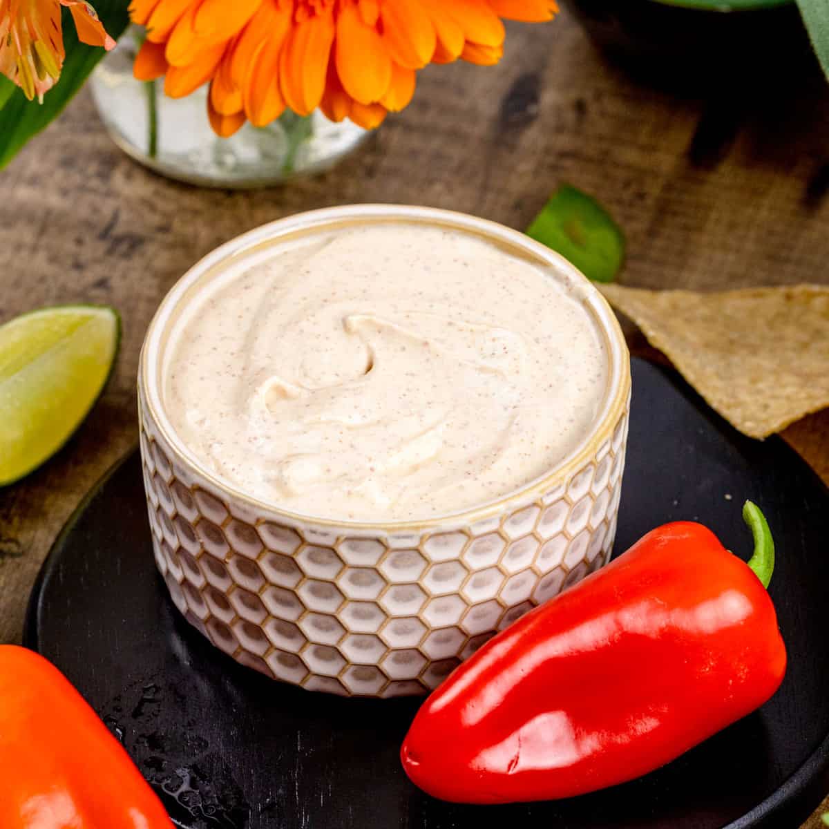 A small bowl filled with fresh dairy free chipotle crema sauce. Fresh red peppers surround the bowl.