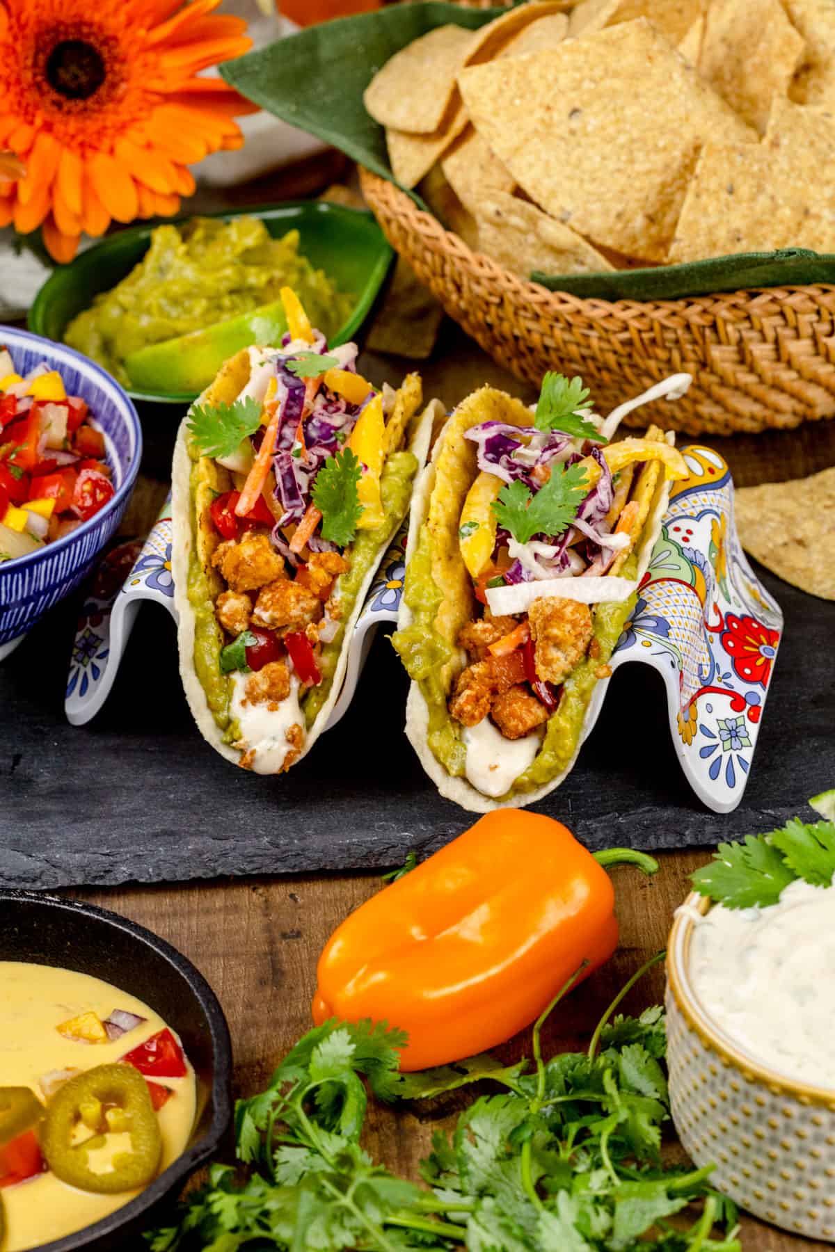 A tables cape for taco night filled with tortilla chips, tofu tacos, salsa, dairy free cheese sauce, and more.