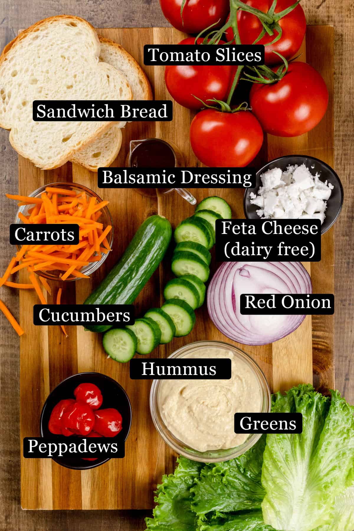 The ingredients for a Panera copycat Mediterranean Veggie Sandwich on a wood cutting board. Black and white labels have been added to name each ingredient.
