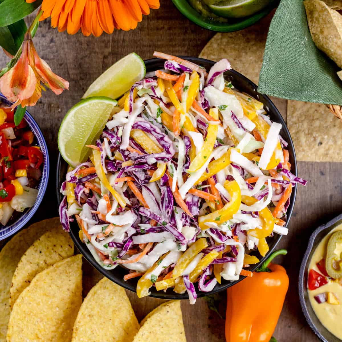 A big bowl of jicama cabbage coleslaw on a wood tabletop surrounded by fresh ingredients for taco night.