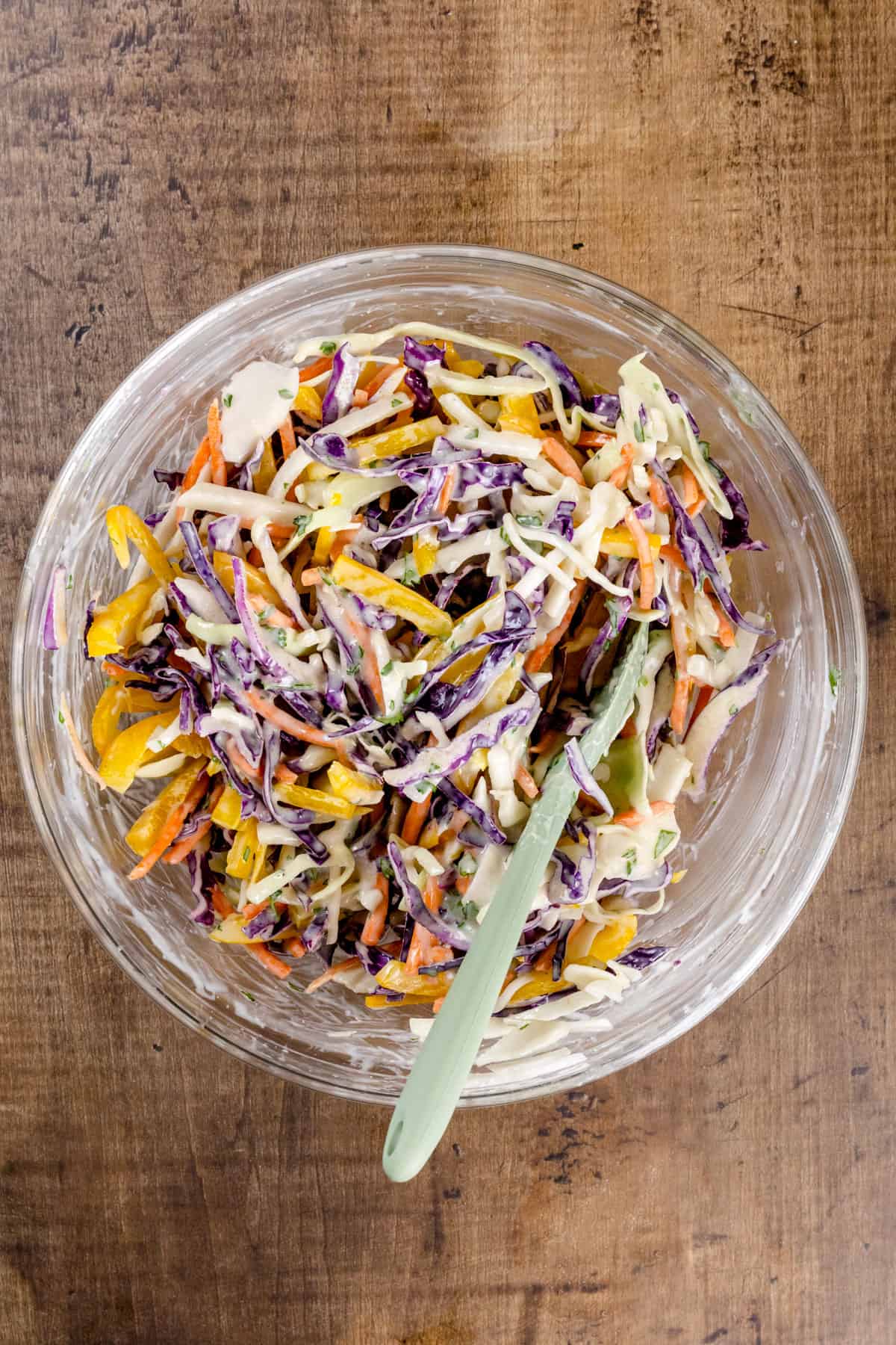 A glass bowl filled with the fully mixed coleslaw on a wood tabletop.