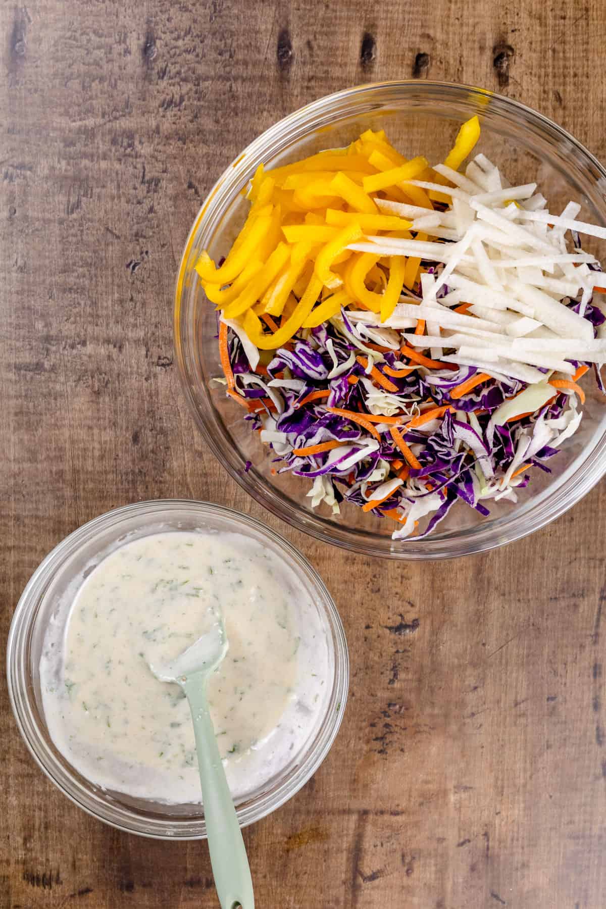 Two glass bowls, one filled with the coleslaw dressing and one filled with the coleslaw mix.