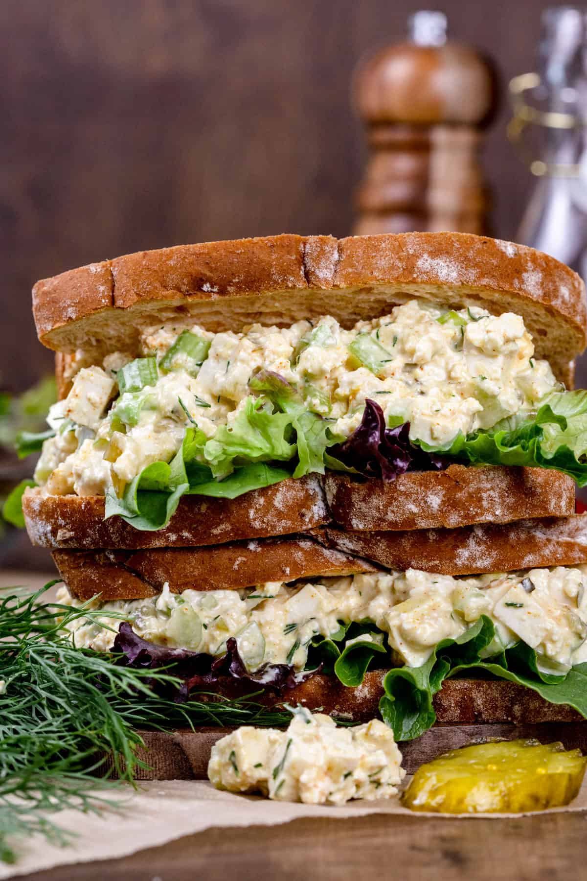 A double stacked sandwich filled with vegan egg salad mixture with lettuce and pickles next to it.