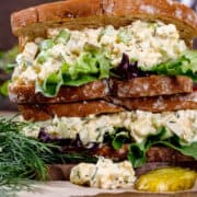 Close up of a stack of sandwiched filled with vegan tofu egg salad, green leaf lettuce, and pickles.