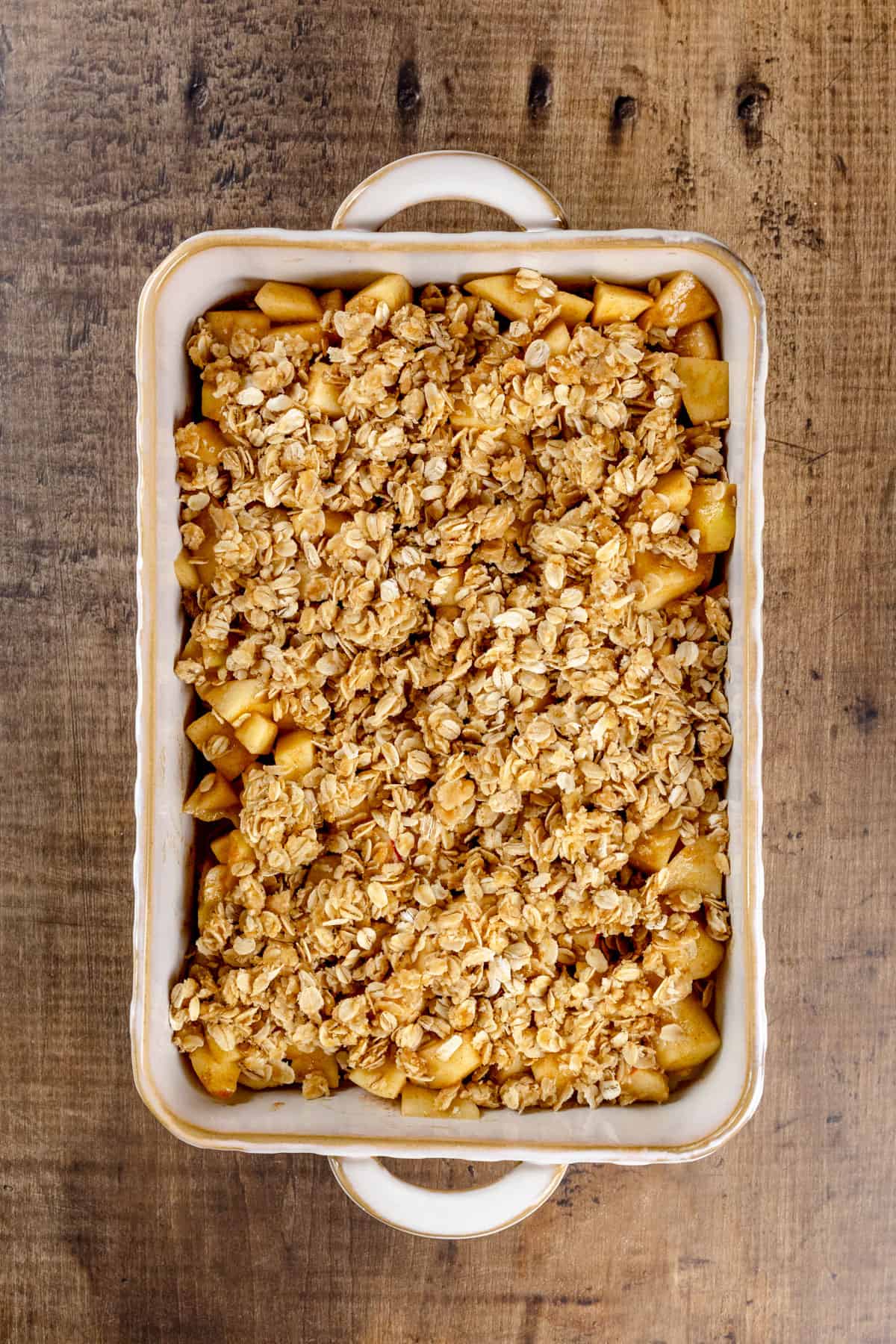 Apple crisp before baking in a ceramic baking dish on a wood table.