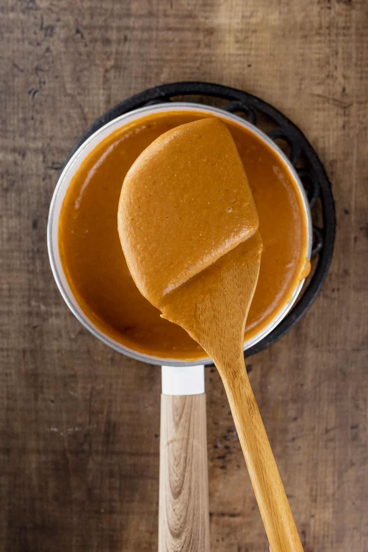 A wood spoon is holding up a spoonful of queso after cooking to show how thick and yummy it is. 