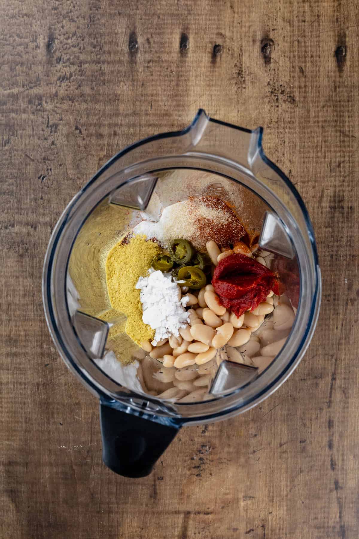 A blender on a wood tabletop is filled with the ingredients to make dairy free queso. This is before the ingredients have been blended so you can see all the ingredients.